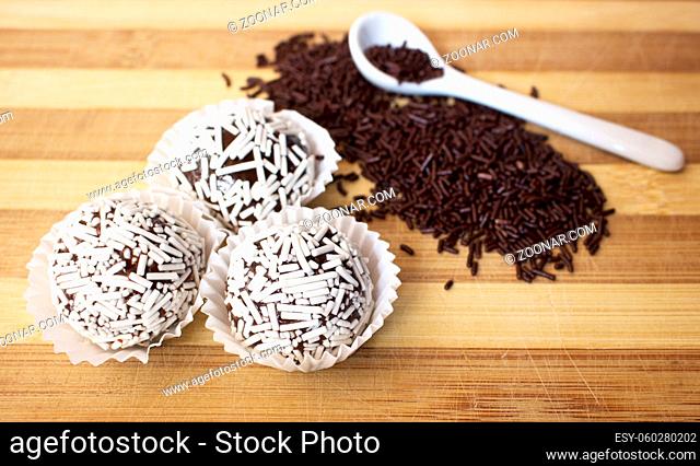 Horizontal photo of Brazilian brigadeiro delicacy with white sprinkles in wooden table, with white spoon on top of chocolate sprinkles