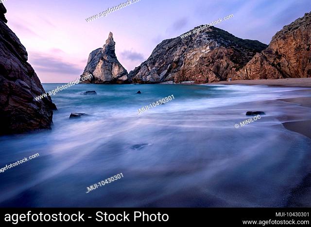 Epic Ursa Beach, Sintra, Portugal. Beach with waves and jugged rock peak in evening soft sunset light. Atlantic Ocean coast landscape