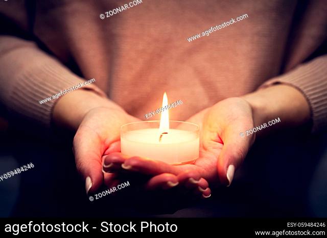 Candle light glowing in woman's hands. Praying, faith, religion concept