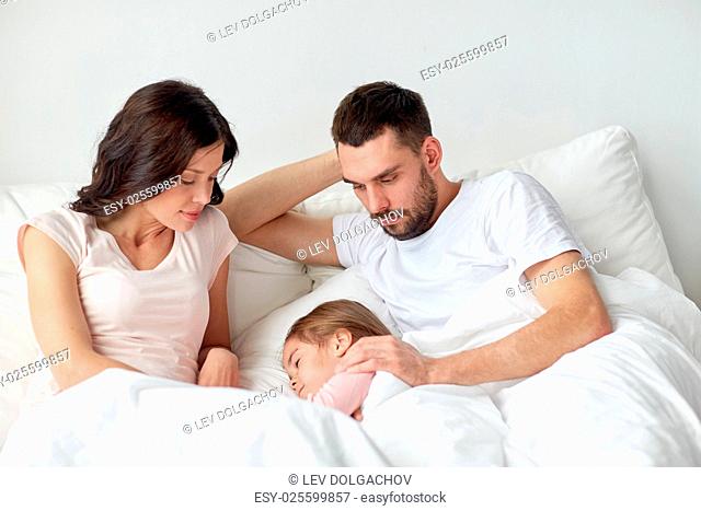 people, family and rest concept - child sleeping with parents in bed at home