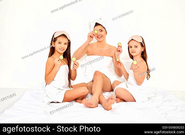 smiling woman with her daughters in white towels holding fresh cucumber slices