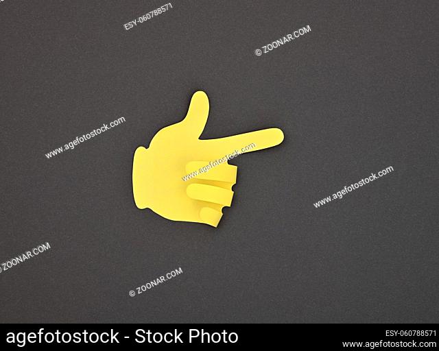 Paper made yellow hand gesture sticker pointing with index finger over grey background