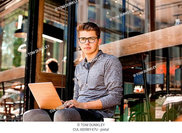 Young man using laptop at cafe, London, UK