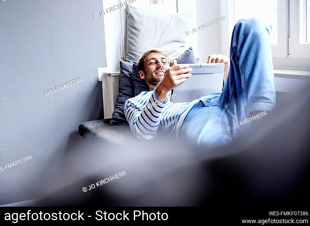 Smiling businessman using tablet PC lying on sofa at home