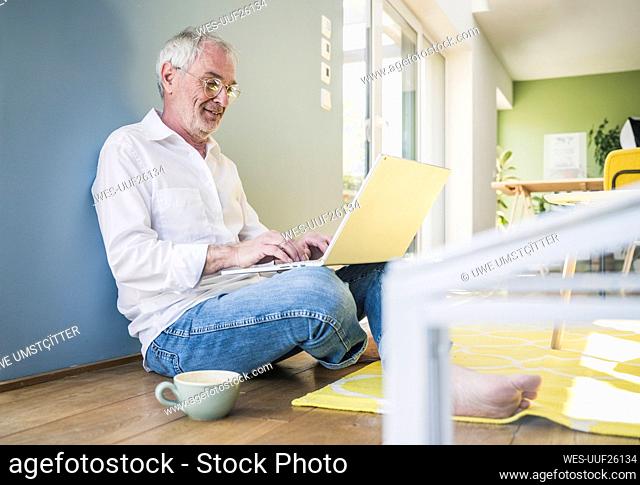 Smiling senior man wearing eyeglasses using laptop at home