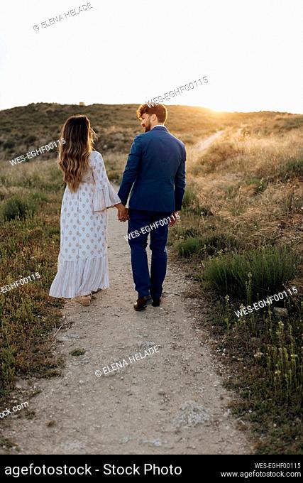 Couple holding hands while walking together during sunset