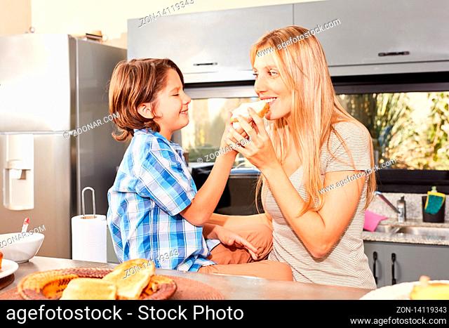 Junge füttert seine Mutter mit Scheibe Toast morgens beim Frühstück in der Küche