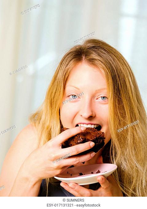 Photo of a beautiful blond woman in her early thirties with log blond hair eating a large piece of brownie or cake