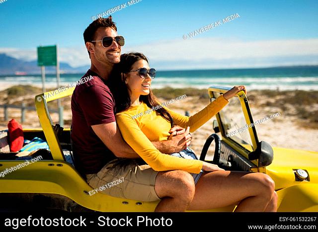 Happy caucasian couple sitting on beach buggy by the sea embracing