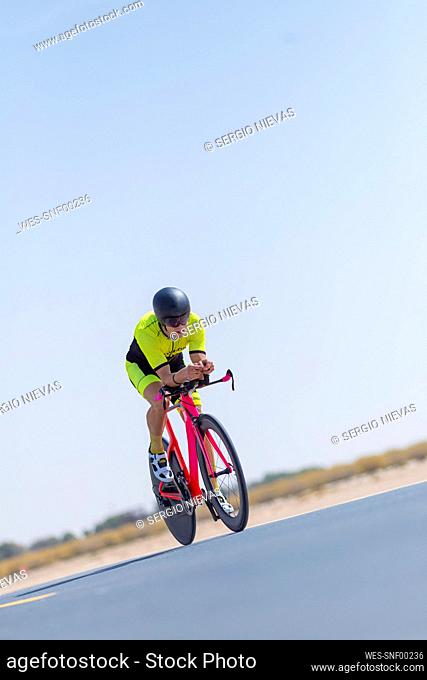 Determined cyclist riding bicycle on road against clear blue sky, Dubai, United Arab Emirates