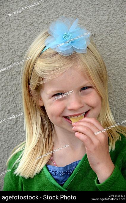 Portrait on a smiling blond girl, 5 years old, who eats a cake in Ystad, Sweden, posing with a hair decoration