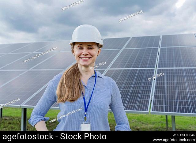 Smiling mature engineer wearing hardhat standing in front of solar panels