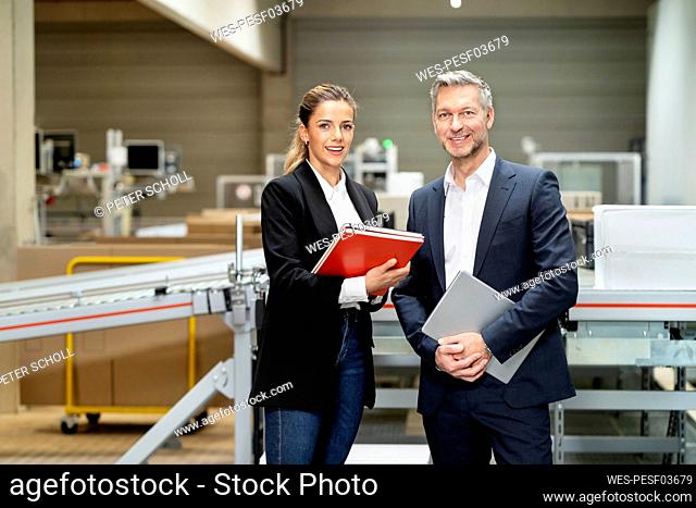 Smiling young businesswoman with businessman in factory