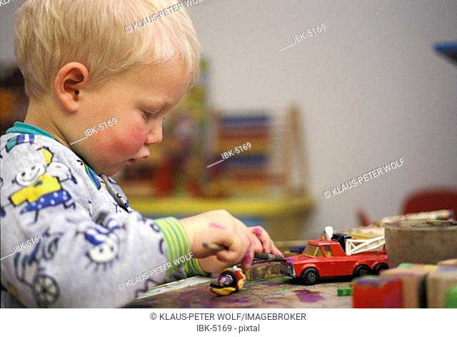 Little one year old boy painting toy fire car