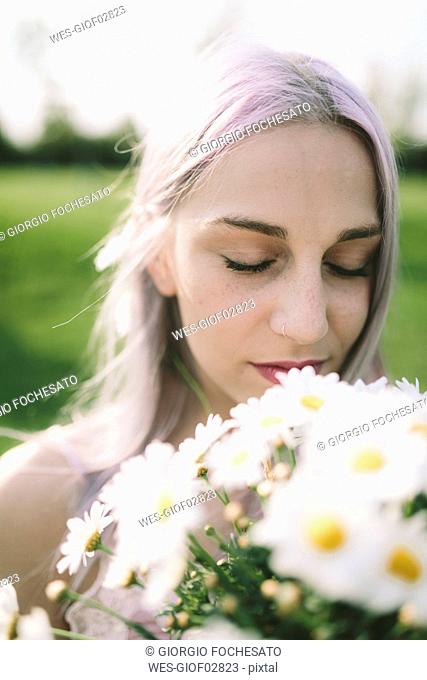 Woman with eyes closed holding bunch of daisies