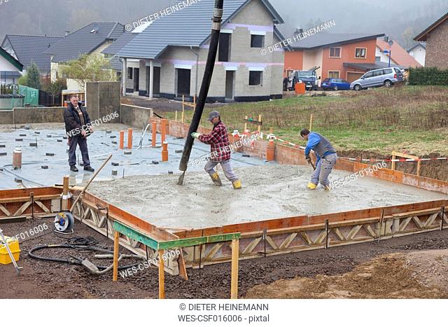 Europe, Germany, Rhineland-Palatinate, Construction workers filling concrete for foundation and man holding remote control
