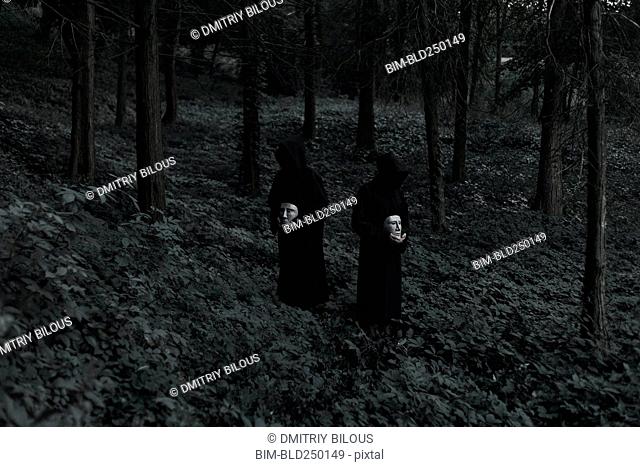 People wearing black robes and holding white masks in forest