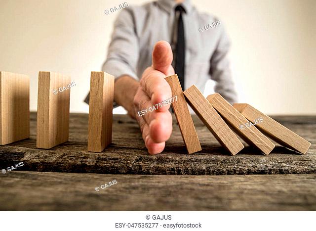 Businessman halting the domino effect inserting his hand between falling and upright wooden blocks in a close up conceptual image