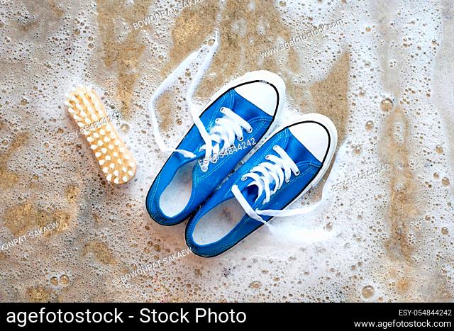 Sneakers with foam of powder detergent water dissolution and wooden brush on cement floor. Washing dirty shoes. Top view