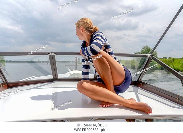 Netherlands, Limburg, Osen, Meuse river, woman sitting on upper deck of a sailing yacht