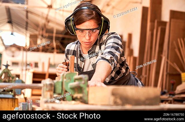 Junge Frau arbeitet als Schreiner oder Handwerker in einer Werkstatt mit Holz