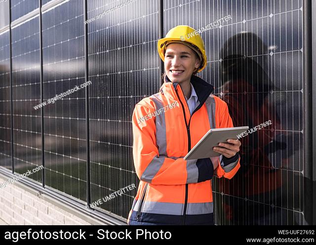 Happy female engineer with tablet PC leaning on solar panels