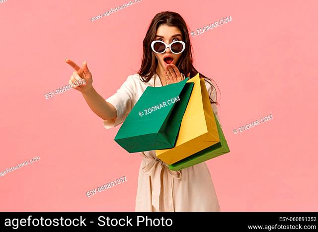 Shoppaholic, shopping and consumer concept. Excited and amused young brunette pretty woman checking out amazing discounts while strolling stores, holding bags