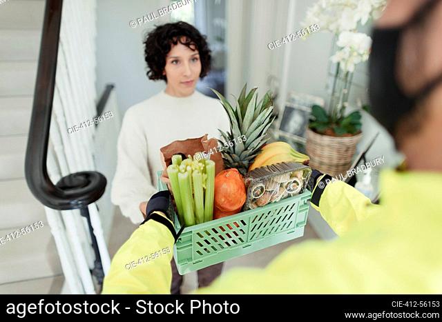 Woman receiving grocery delivery from courier in face mask