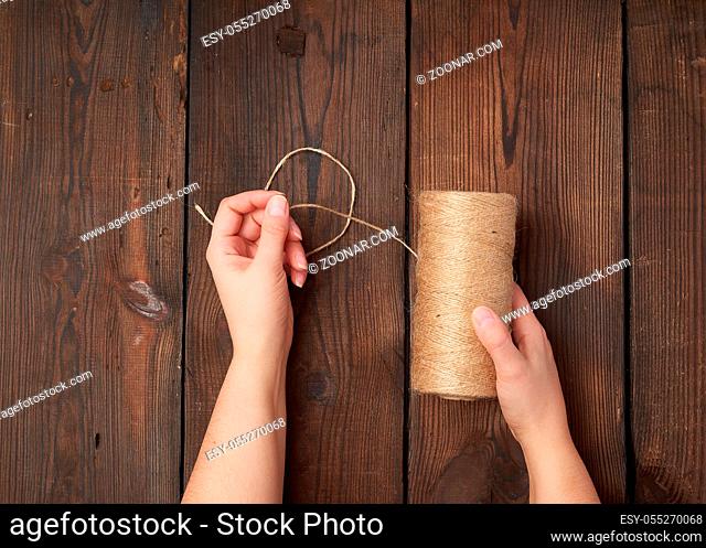 female hands holding a skein with brown eco thread on a brown wooden background, top view