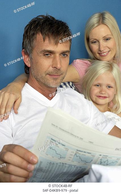 Father lying in bed with daughter and wife and is reading a financial paper, close-up