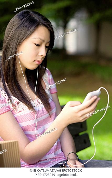 A young woman sitting on a park bench listening to her music player