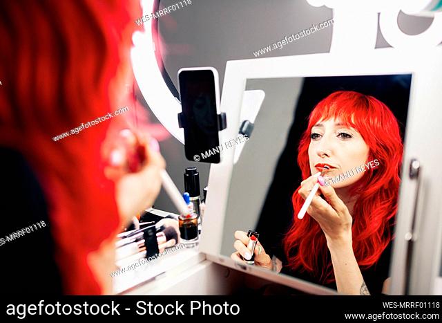 Female vlogger applying lipstick while looking at reflection in mirror in studio
