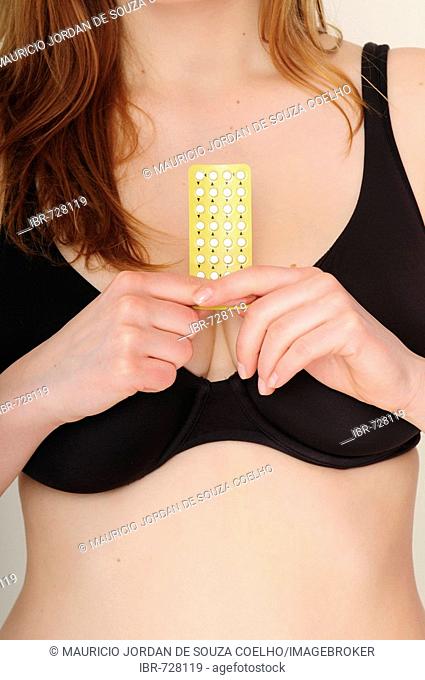 Young long-haired woman wearing black bra holding a pack of birth control pills