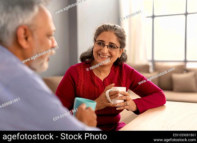 AN OLD WOMAN HAPPILY LOOKING AT HUSBAND DURING TEA TIME