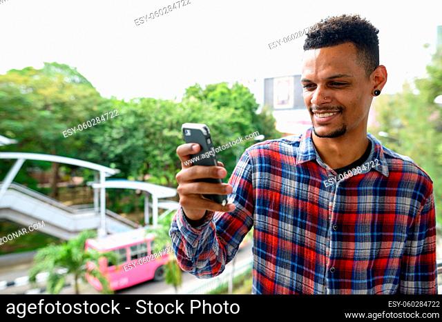 Portrait of young handsome bearded African hipster man against view of the city streets outdoors