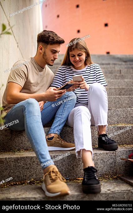 Couple using mobile phones while sitting on steps