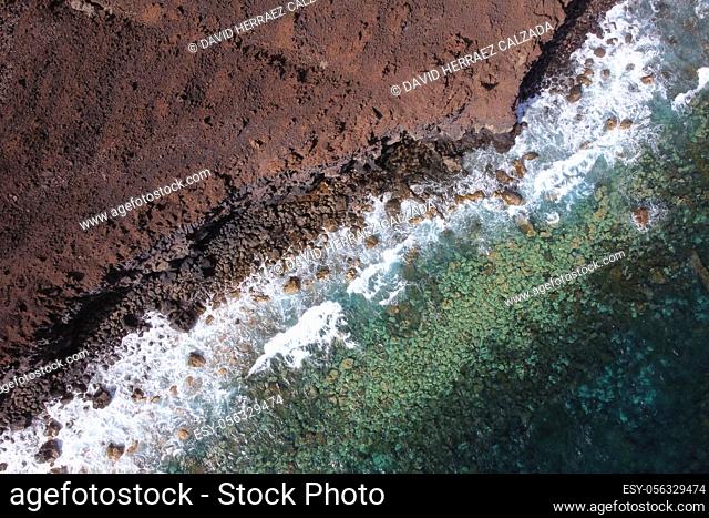 Aerial top view of waves splashing on rocky volcanic coastline. High quality photo
