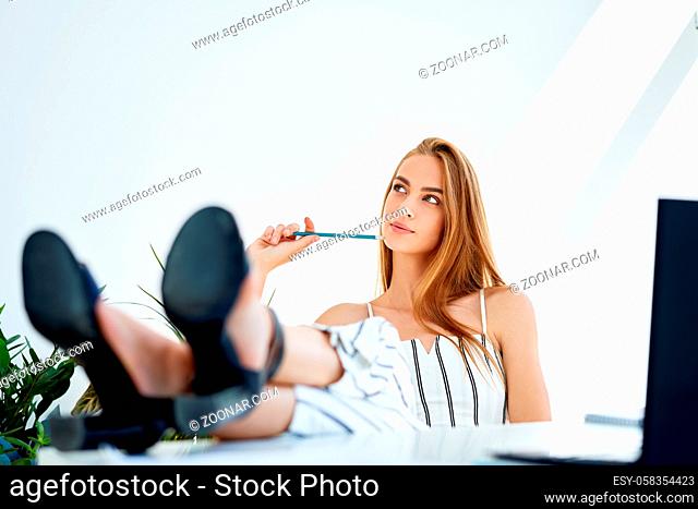 Thoughtful pretty young businesswoman relaxing in modern office with legs on the table enjoying free time. Relax concept. Break time