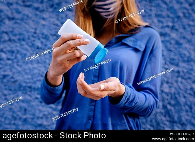 Close-up of young woman washing hands with sanitizer against blue wall in city
