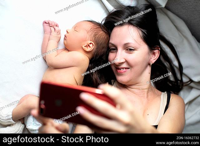 Close-up of a mother and her newborn baby taking a selfie or video call to their father or relatives in bed. Technology concept, new generation, family
