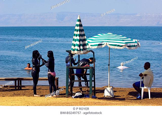 four teenage tourists putting black medical mud onto their whole bodies at a beach at the Dead Sea, Jordan