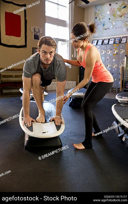 A yoga instructor helping a student with a yoga pose on top of a surfboard exercise machine