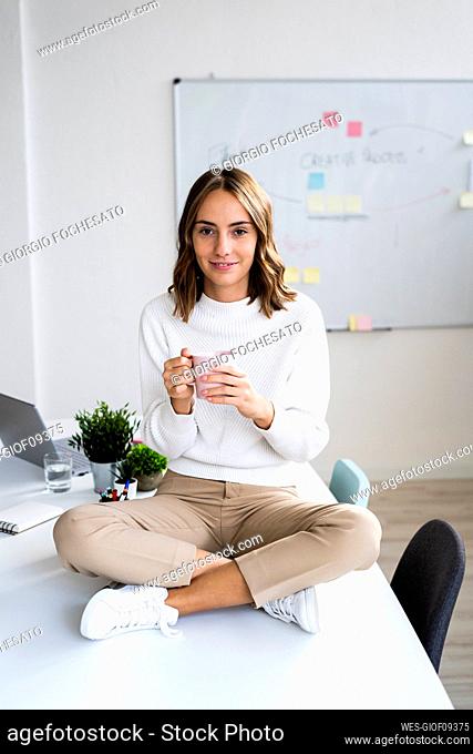 Young businesswoman drinking coffee while sitting on table at office