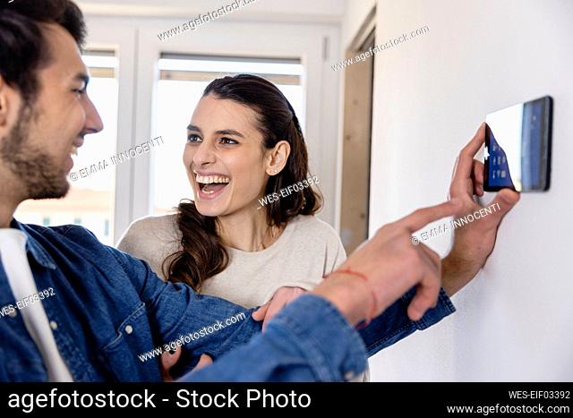 Cheerful woman talking with boyfriend holding tablet PC at new home