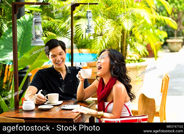 Asian man and woman in restaurant or cafe having fun drinking hot beverage