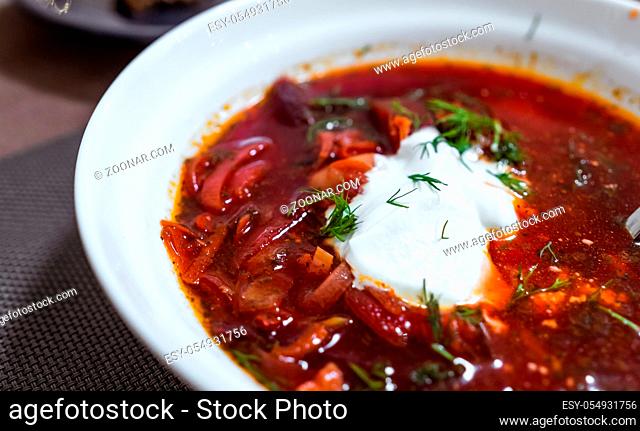 Cooked red borsch with sour cream in a white plate, close veiw