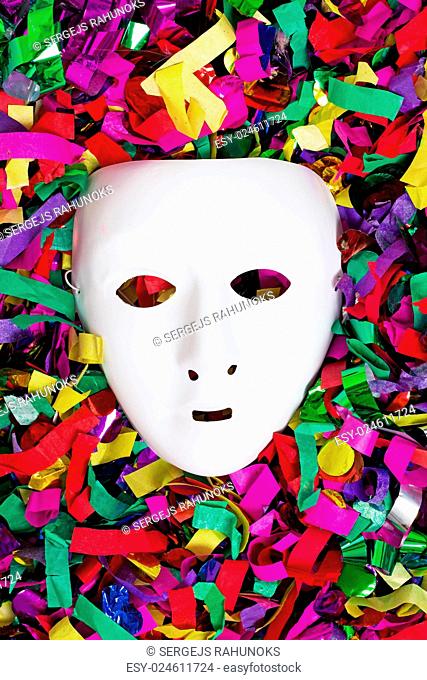 Picture of a white mask that is lying on colorful streams and confetti