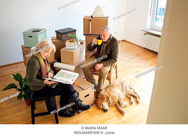 Senior couple having a break surrounded by cardboard boxes in an empty room