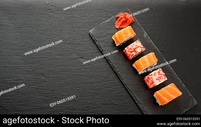california sushi with red tobiko caviar and slices of philadelphia sushi on black slate board, top view