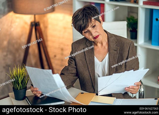 Working on project. Short-haired businesswoman sitting in the office and working with papers